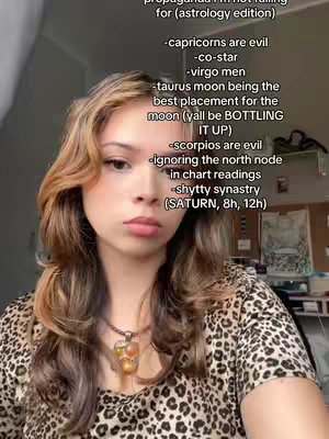A young woman with long, wavy auburn hair is centered in the frame. She wears a patterned top and a necklace with a large pendant. Text overlays on the right side list opinions on zodiac signs.