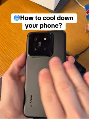 A person holding a black smartphone, presenting it with their hands, with a white overlay containing the text 'How to cool down your phone?' and a small icon of a cold face.
