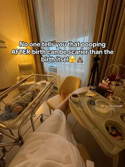 A woman's perspective in a hospital room after giving birth. The image is shot from a low angle, focusing on the woman in a hospital bed who is wearing a patient gown and is angled down as she holds the camera. A baby can be seen sleeping inside a clear bassinet to the left. A tray table with food is in the foreground. Text overlay highlights concerns around post-birth bowel movements.