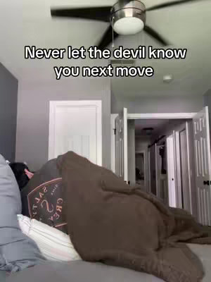 A person is lying in bed, partially covered by a brown blanket. Above, text provides the video's hook. The room has grey walls and a ceiling fan. The door and a portion of its doorway are visible to the right, indicating another room beyond.