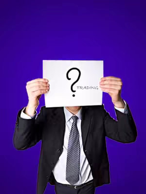 A person in a suit holding up a white paper that is covering their face, on the paper is a question mark with the word trading written under it. The background is a shade of purple.