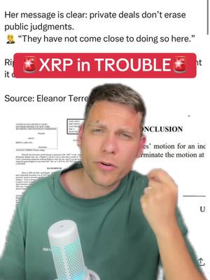 A man with short, light hair is centered in the frame, looking directly at the camera. He's wearing a green t-shirt and holding a microphone with a blue and white striped handle. Behind him are documents and text, plus an overlaid hook that says "XRP in TROUBLE." The background suggests a news update or financial analysis.