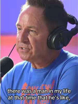The image shows a man in his late 30s or early 40s with short brown hair, wearing a blue shirt and black headphones around his neck, speaking into a microphone. The image is lit with pink and purple lights. The overlay text is white and appears in a lower third position.