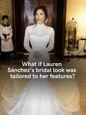 A vertical shot features a woman in a white wedding dress set against an indoor background. The woman is the central focus, standing and posing, facing the viewer. The dress has a high, lace-detailed neckline, long sleeves, and a full skirt that spreads out on the floor. The background is softly blurred and features an architectural interior, with a glimpse of another person and an adjacent decorative item.