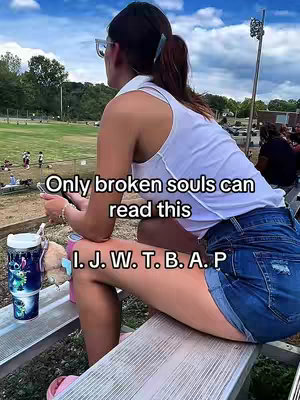 A woman in a white tank top and jean shorts is sitting on a bench, looking away from the camera. Text overlays read, 'Only broken souls can read this' and 'I. J. W. T. B. A. P'. The background shows a green field and a blue sky.