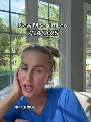 A woman with blonde hair and a blue shirt sits in front of a large multi-paned window with trees visible outside. Text overlays read "New Moon in Leo 7/24/2025" and "OUR NEW MOON".