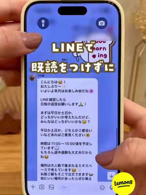 A smartphone screen displays a LINE chat conversation with Japanese text. The phone itself is held by a person with manicured nails. The background is blurred, suggesting an indoor setting.