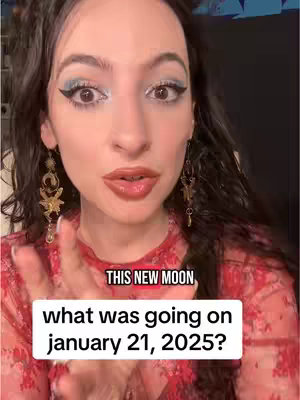 A woman with long dark wavy hair, makeup, and large earrings is centered in a selfie-style shot, with text overlays below. She gestures with her hands towards the camera. The background is dark, and the woman’s dress is red and patterned.