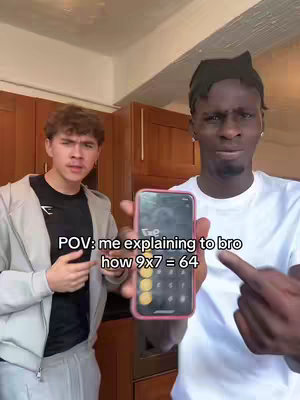 Two young men stand in a kitchen setting. One holds a phone displaying a calculator, and points at it with a questioning expression. The other looks on with an expression of disbelief or confusion. Text overlays the scene.