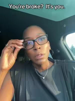 A woman with short hair and glasses looks directly at the camera. The background is blurred, suggesting the video is being filmed in a car. Overlayed text reads, "You're broke? It's you."