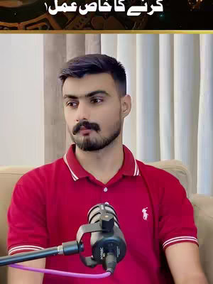 A man with a beard and mustache wearing a red polo shirt sitting on a tan couch, holding a microphone. Text in Urdu is at the top, with a subtle gold border.