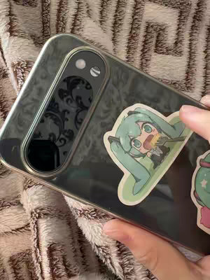 The cover image shows a close-up shot of a smartphone, angled to display its back. The phone is encased in a clear case. There is a sticker of a manga-style character with teal hair. The surface beneath the phone appears to be a textured, tan-colored fabric.