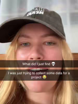 A selfie-style image featuring a young woman wearing a baseball cap and looking at the camera with a surprised expression. A text overlay is present, stating "What did I just find" and "I was just trying to collect some data for a project". The background is softly blurred, likely a room interior. The overall composition frames her face prominently, with the text overlay adding context and emphasis.