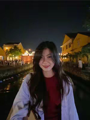 A woman smiles in front of a historical canal with yellow buildings, bridges, and lights at night.