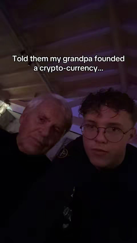 Two men are featured in a selfie-style shot. An elderly man with white hair and a younger man with glasses share the frame, both gazing towards the camera in a domestic setting. The text overlay reads: 'Told them my grandpa founded a crypto-currency...'.