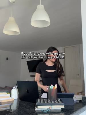 The image shows a woman in a black top standing in front of a countertop with a laptop. Overhead two white lamps are visible. Text overlay reads, "if you fail, no one will care why they will just know you FAILED."