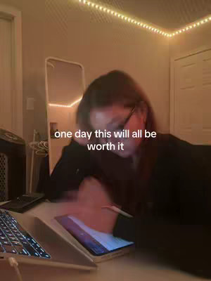 The image shows a dimly lit room with a person seemingly studying on a laptop and a tablet. The words \"one day this will all be worth it\" are overlaid on the image, acting as the hook. The color scheme leans towards warm tones due to the ambient lighting. The setting appears to be a bedroom or a personal study space.