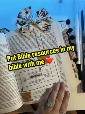 A close-up shot of an open Bible with a floral bow on top. The text overlay reads, "Put Bible resources in my bible with me". A red heart emoji is included. The bottom right of a hand with rings is visible.