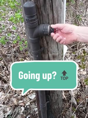 The image shows a wooden pole with a black pipe apparatus attached. A hand is turning a red valve on the pipe. A speech bubble with the text 'Going up?' and an upward arrow adorn the bottom left corner.