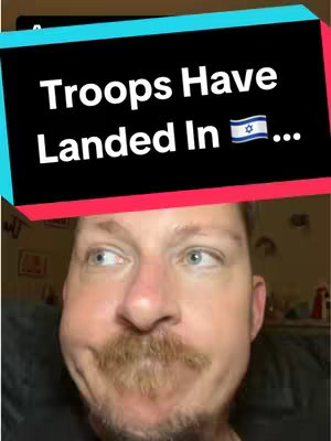 A man with fair skin gazes off to his left side with a slight smile and one raised eyebrow. Above him is a black rectangle with white text that reads: "Troops Have Landed In" followed by the Israeli flag and three dots.