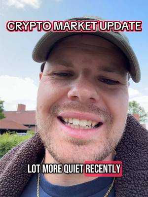 A selfie shot of a man, taken from the chest up. The man has fair skin, short, light-brown hair, stubble, and a slight smile. He's wearing a dark cap and a dark, textured top. Text overlays appear in bold, white font against transparent red rectangles. The background is slightly blurred, showing foliage and buildings.