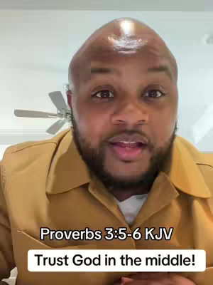 A close-up shot of a man with a shaved head and a trimmed beard, wearing a light brown collared shirt. The image features text overlays at the bottom, within a white and black box. The background is simple, with a ceiling fan visible.