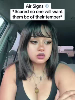 A woman, framed from the chest up, with fair skin, dark hair, and bangs, is seated inside of a car. Above her head is a text overlay that reads "Air Signs" with a cloud symbol. Beside this text it says "*Scared no one will want them bc of their temper*". The woman is looking toward the viewer, with a concerned expression. She wears a black top and a necklace. The background is softly out of focus.