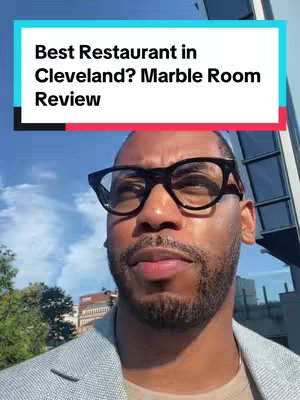 The cover image features a close-up of a Black man wearing black-rimmed glasses. He appears to be outdoors, with a bright, sunny sky providing the background. A text overlay in a white box with a teal outline is positioned above his head, with the text "Best Restaurant in Cleveland? Marble Room Review".
