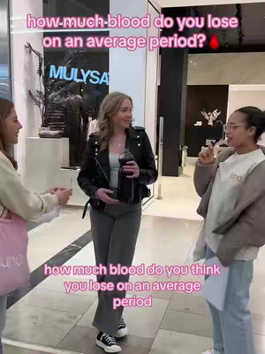 Three young women stand indoors conversing. The central figure holds a drink, while two others gesture as if in conversation. Text overlays in pink and white fonts pose questions regarding periods. The setting appears to be a store entrance based on the exterior views shown in the background.