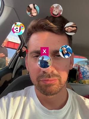A selfie taken from inside a car featuring a man with brown hair and a short beard. The man is wearing a white t-shirt and is centered in the frame. Around his face are a series of circular profile pictures of other people. Overlaying his face is a pink rectangle with the letter \"X\" in white. The background appears to be the inside of a car.