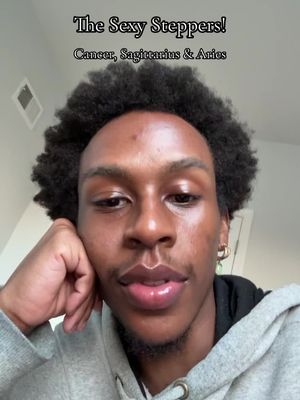 A selfie-style shot featuring a young Black man with dark, curly hair. He looks directly at the camera with a slight smile, supporting his head with one hand. The background is neutral, and text overlays at the image’s top indicate the video's astrological theme.