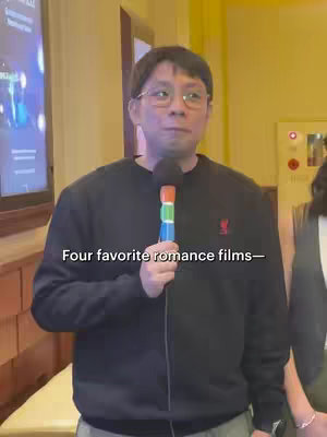 The cover image features a man with glasses holding a microphone, wearing a black sweater. He is positioned in front of a wall with a screen on the left. Another person is partially visible on the right side of the frame. The overall color scheme is warm, with yellow lighting.