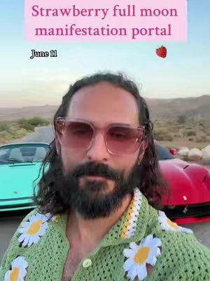 A man with long dark hair and a beard wearing oversized pink sunglasses and a green crocheted shirt with daisy-like flowers is the central focus, set against a backdrop of a road, cars, and a natural landscape under a bright sky. Text overlays add context, focusing on astrological themes.