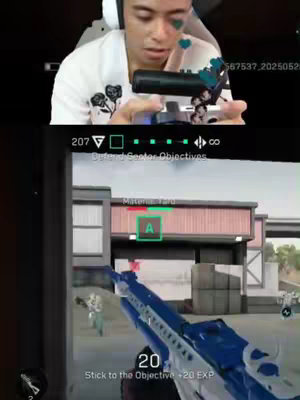 The cover image is split into two sections. The top half shows a person wearing a white shirt with a small black floral pattern, a headset, and a visible microphone. This person has a small dark blue heart emoji on their finger and face. The bottom half portrays a first-person perspective from a video game, showing a gun aiming at an outdoor setting. The game interface displays health, the objective, and the score.