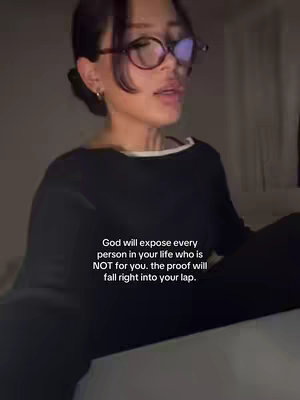 A woman with dark hair wearing glasses and a black top is looking slightly up towards the viewer; text appears below her.