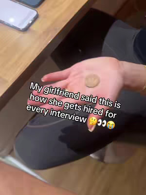 A close-up shot of a hand holding a coin against a background. Text overlay states, "My girlfriend said this is how she gets hired for every interview" with emoji.