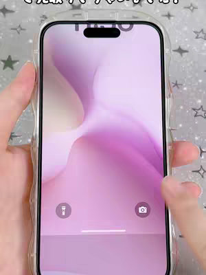 A person holds a phone, displaying a customized lock screen with a pastel purple and white gradient wallpaper. The phone is in a clear case, and their fingers partially obscure the display.