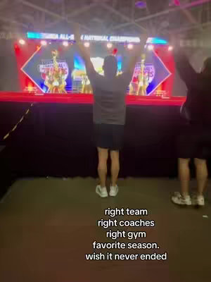 The cover image shows an individual with their arms raised, facing away from the camera. In the background, a cheerleading competition stage is visible, with other individuals on stage. Overlayed text at the bottom provides commentary about the scene.