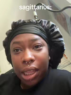 A close-up shot features a person looking toward the camera with a slight smile. The individual is wearing a black bonnet and a dark top, with noticeable piercings on the nose and lower lip. The background is blurred, with a soft, muted palette. The overall composition focuses on capturing a personal and intimate moment.