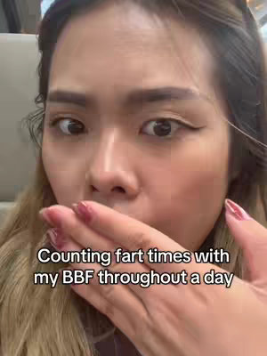 A close-up shot of a woman covering her mouth with her hand, revealing red nail polish. The image is set in a somewhat unfocused background. Text overlay at the bottom of the frame reads: "Counting fart times with my BBF throughout a day".