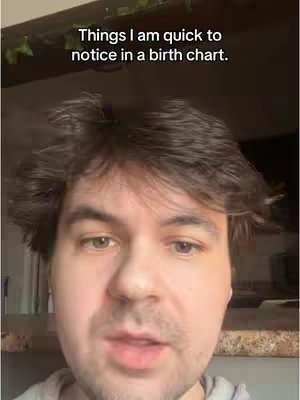 A medium close-up shot of a man's face, centered in the frame. The man has light skin, short brown hair, and appears to be looking directly at the camera. His eyes are open, and he has a neutral expression. Above him is text overlaid on the image, and the background is blurred, with some greenery visible at the top. The lighting seems natural.