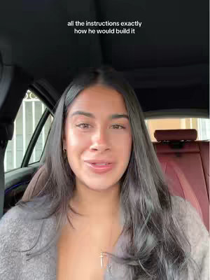 A woman with long dark hair sits in a car. The text overlayed above her head that reads, 'all the instructions exactly how he would build it'. Inside the car the seats are brown.