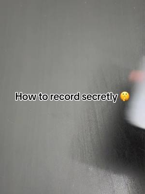 The image has a gray background and black text in the center that says 'How to record secretly' along with a thinking face emoji next to it. Part of an object is visible on the right which appears to be white.
