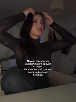 A woman with dark hair is shown in a softly lit room. She is wearing a dark, possibly transparent, long-sleeved top and is touching her hair while looking upward. Text overlayed provides a quote.