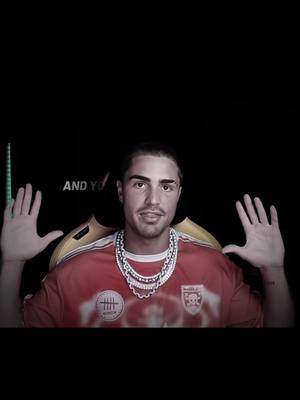 A man with short dark hair wearing a red t-shirt with a white necklace and showcasing open hands. A text appears at the bottom left.