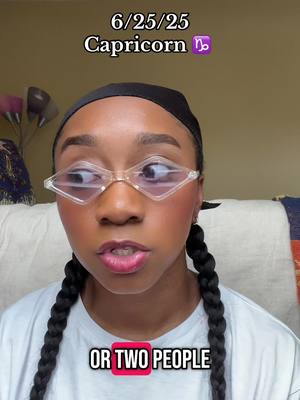 A woman with dark skin and two long, thick braids is the central focus. She has clear, focused eyes behind diamond-shaped, transparent glasses with a light frame. Her lips are lightly tinted with pink lipstick. Above her, text reads '6/25/25' and 'Capricorn ♈', with a purple Capricorn symbol next to it. Below, the text reads 'OR TWO PEOPLE' in a red box. The background has soft, neutral tones with some visible elements like a flower-shaped lamp and patterned fabric, suggesting an indoor setting.