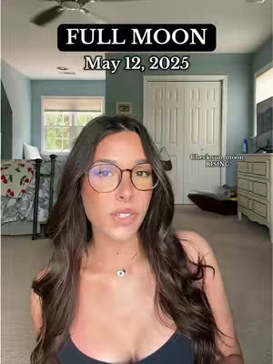 A woman with long brown hair and glasses is the focus of the image. She is in a room with a bed, a window and white doors.
