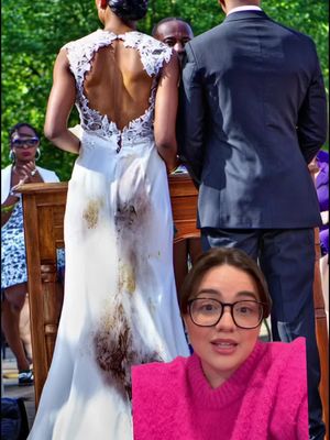 The image shows a bride from the back, wearing a white wedding dress with a detailed lace back and a visible dirt stain on the dress. The bottom part of the dress has a brown stain. A man in a black suit stands beside her. In the foreground, a woman with glasses and a pink sweater is present, looking at the camera.