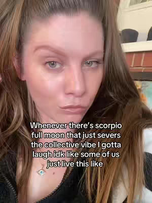 A selfie-style video cover image of a woman with brown hair, looking at the camera with a slight frown. The background is blurred, but hints at an indoor setting. The woman is wearing a dark top and a necklace with a blue eye pendant. Text is overlaid on the image.