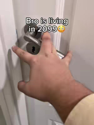 A hand is reaching for a silver door handle on a white door. Text overlayed on the image reads, Bro is living in 2099 with an emoji of a surprised look face.